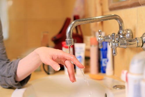 Homeowner testing water pressure at kitchen faucet with pressure gauge