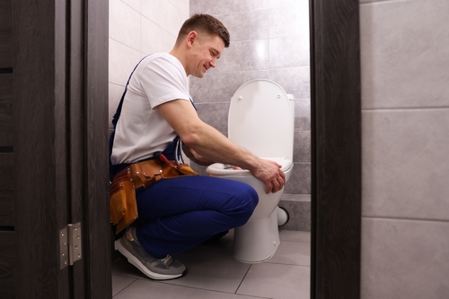 Plumber diagnosing gurgling toilet in residential bathroom